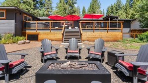 Una zona patio con poltrone Adirondack, un braciere e un edificio con ampie vetrate e ombrelloni rossi.