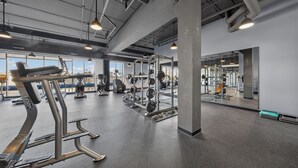 A gym with various exercise equipment, large windows, and a high ceiling with exposed pipes. - Luxury 1 BR I Walk to Mayo Skyway I Pets I Parking (Rochester)