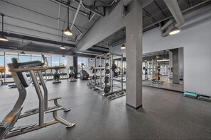 Een sportschool met diverse fitnessapparaten, grote ramen en een hoge ruimte met blootgelegde leidingen.
