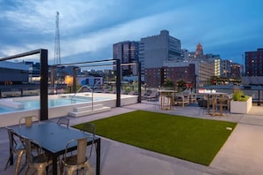 Een terras op het dak met een zwembad, buitenmeubilair en uitzicht over de stad.