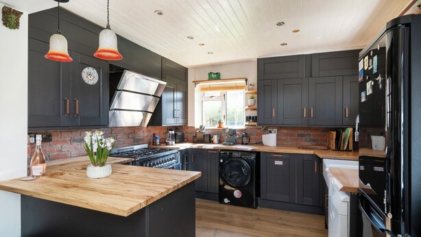 Een moderne keuken met donkere kastjes, een houten werkblad, een roestvrijstalen afzuigkap en een ingebouwde wasmachine.