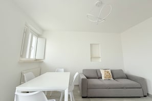 A modern, minimalistic living room with a white table, grey sofa, and a unique ceiling light fixture. - P075 - Porto Recanati, new two-room apartment facing the sea with direct beach access (Porto Recanati)