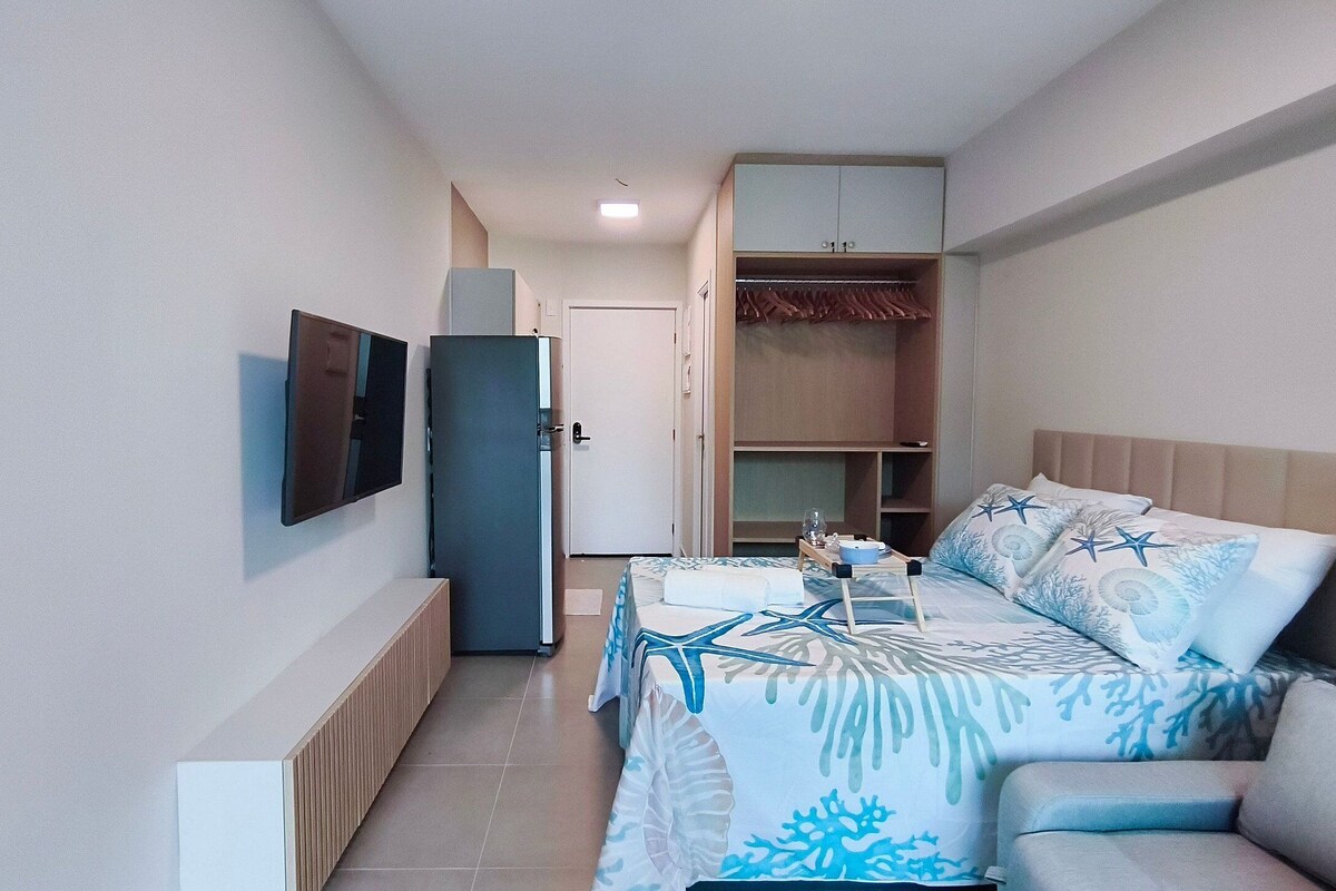 A hotel room with a bed, a TV, a wardrobe, and a small table with a tray.