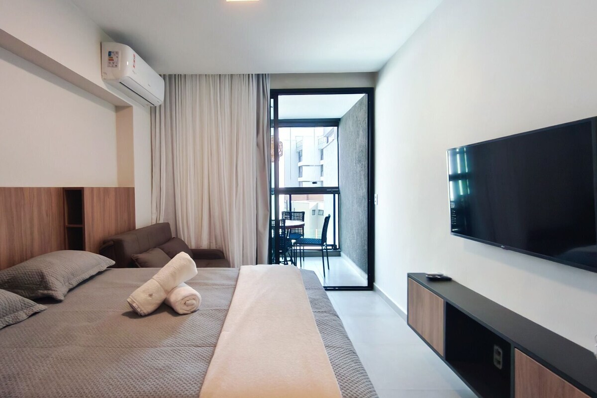 A modern hotel room with a bed, a TV, and a balcony with a view.