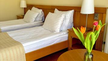 Ein Hotelzimmer mit zwei Betten, einem hölzernen Kopfteil, einem Nachttisch mit Lampe, einem kleinen Tisch mit Blumenvase und einem Bild an der Wand.