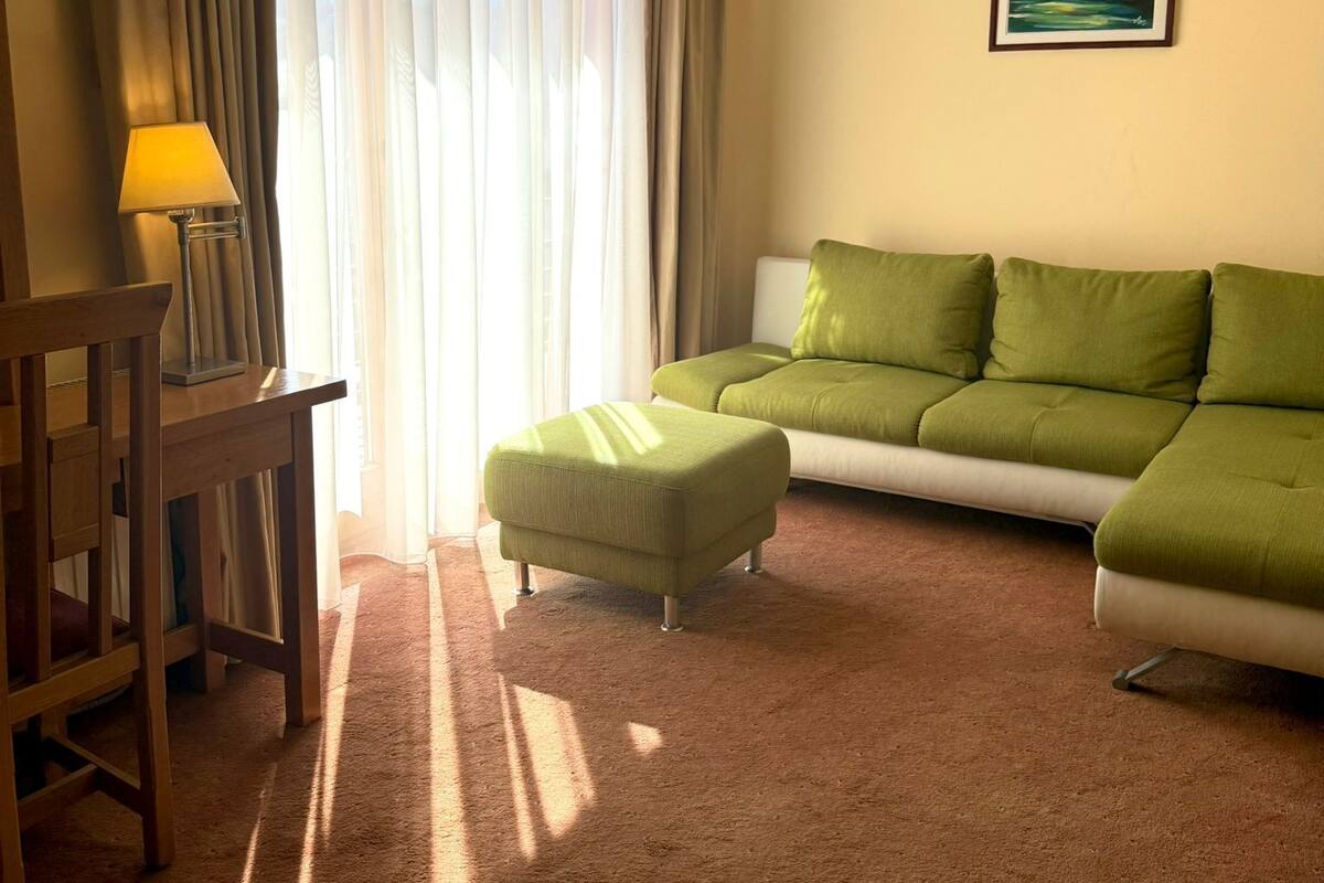 A room with a sofa, an ottoman, a lamp, and a painting on the wall.