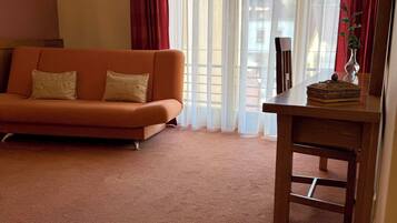 Una habitación con sofá, una mesa con una bandeja de café, un florero con una flor y una ventana con cortinas.