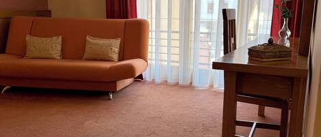 A room with a sofa, a table with a tray of coffee, a vase with a flower, and a window with curtains.