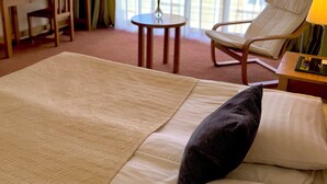 Habitación de hotel con una cama grande, un escritorio, una silla, una mesita con un jarrón y vistas por la ventana.