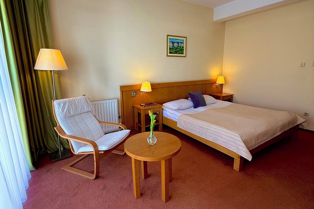 A hotel room with a single bed, a chair, a small table, and a lamp.
