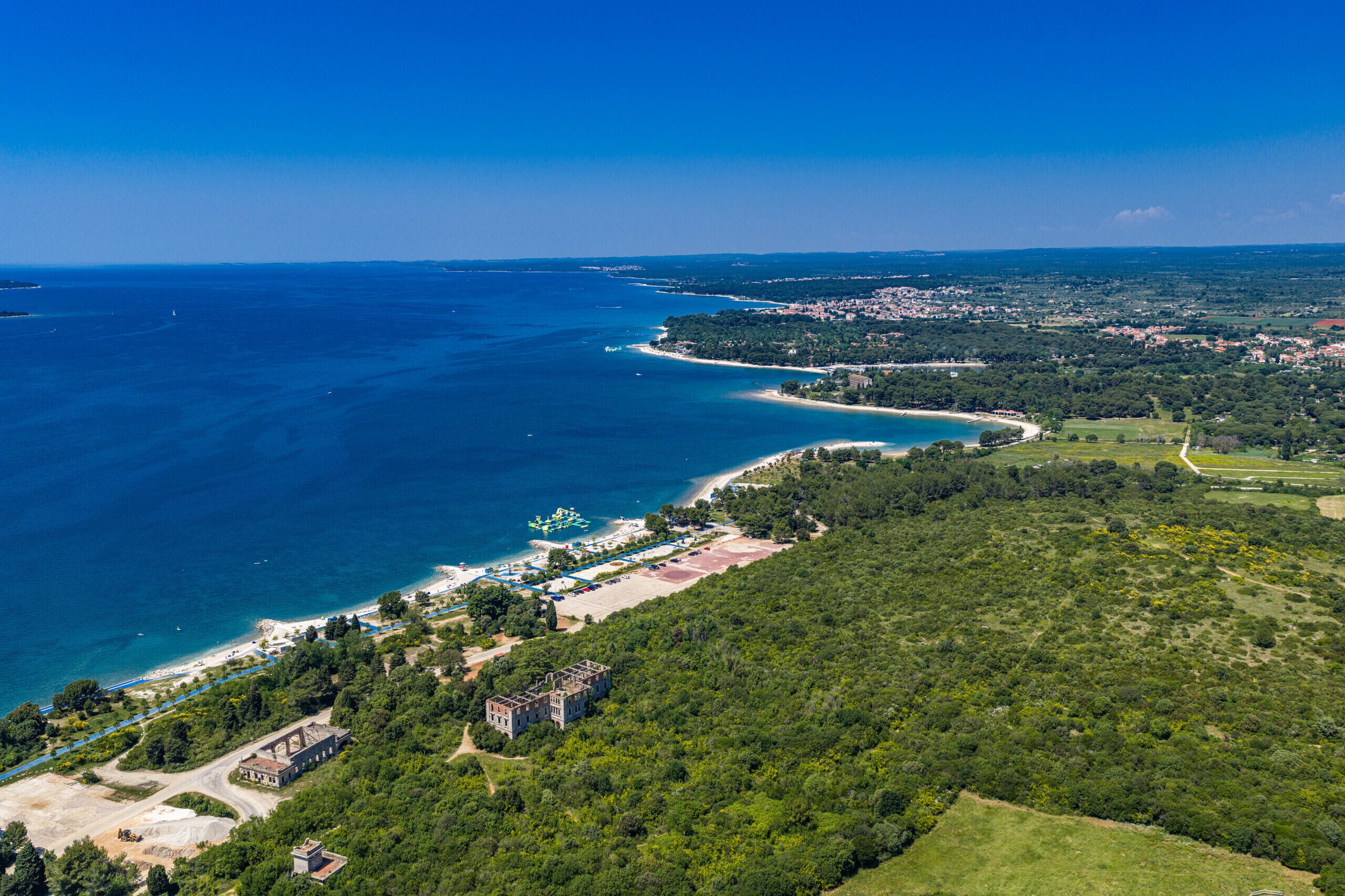 Ein Luftbild einer Küstenlandschaft mit Strand, bewaldetem Hügel und einem kleinen Gebäude.