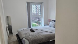 Ein Schlafzimmer mit Bett, Fenster, Lampe und Tür.