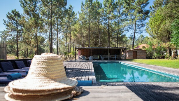 Um deck de madeira com piscina, espreguiçadeiras e um chapéu de palha.