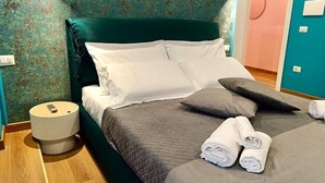 A neatly made bed with pillows, a bedside table with a remote control, and a wall with a floral pattern. - MARILU' ACCOGLIENZA DEL SUD (Foggia)