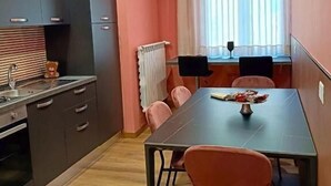 A compact kitchen with modern appliances, a dining area with a table and chairs, and a window with curtains. - MARILU' ACCOGLIENZA DEL SUD (Foggia)