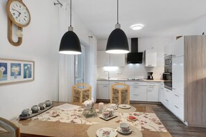 Una cuina moderna amb armaris blancs, una taula de dinar de fusta i separadors de taula amb motius florals, i il·luminació penjant.