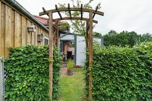 Una pèrgola de fusta en un jardí, amb un camí de rajola que mena a un edifici.