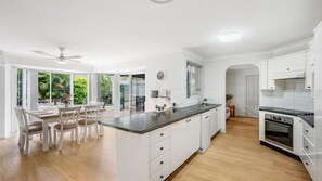 Une cuisine moderne avec des meubles blancs, un îlot central et un coin repas offrant une vue sur la verdure.