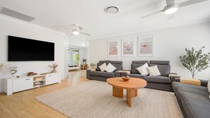 A modern living room with a flat-screen TV, grey sofas, a wooden coffee table, and a large window. - Skye at Lighthouse, 2 Skye Court (Port Macquarie)