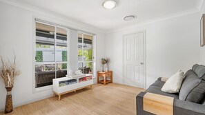 Ein Zimmer mit großem Fenster, einer Couch, einem kleinen Tisch und einer Tür.