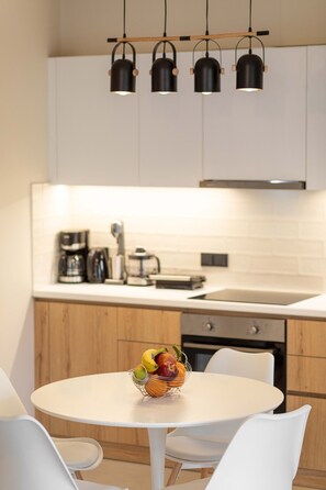 A modern kitchen with white cabinets, a round dining table, and a fruit basket. - Olivevine 5 - Luxury Apartment With Nafplio View (Nafplio)