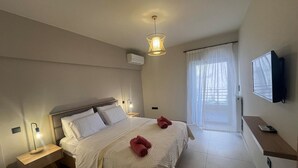 Hotellihuone, jossa on sänky, yöpöytä, lamppu ja seinälle asennettu televisio.