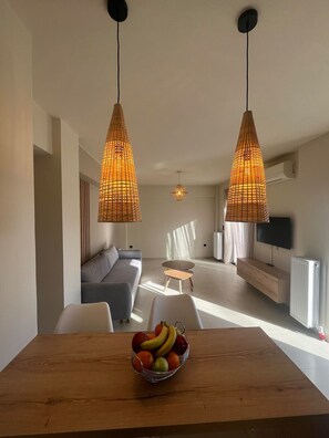 Ein modernes Wohnzimmer mit einer Couch, einem Esstisch mit Obst und zwei Pendelleuchten.