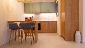 A modern kitchen with wooden cabinets, a central island with stools, pendant lighting, and a white vase on the floor. - Olivevine4 (Nafplio)