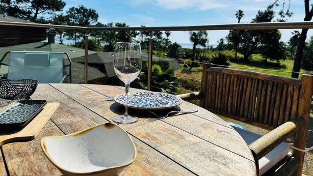 Un tavolo di legno con un bicchiere di vino, piatti e ciotole su un balcone con vista su un paesaggio suggestivo.