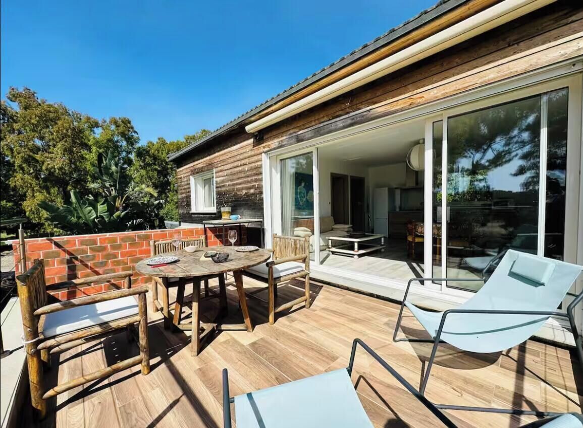 An outdoor patio with a wooden table and chairs, a glass door leading to an interior space, and a brick wall.