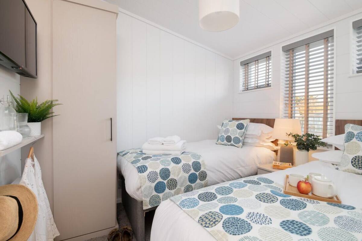 A bedroom with two beds, a TV, a lamp, and a window with blinds.