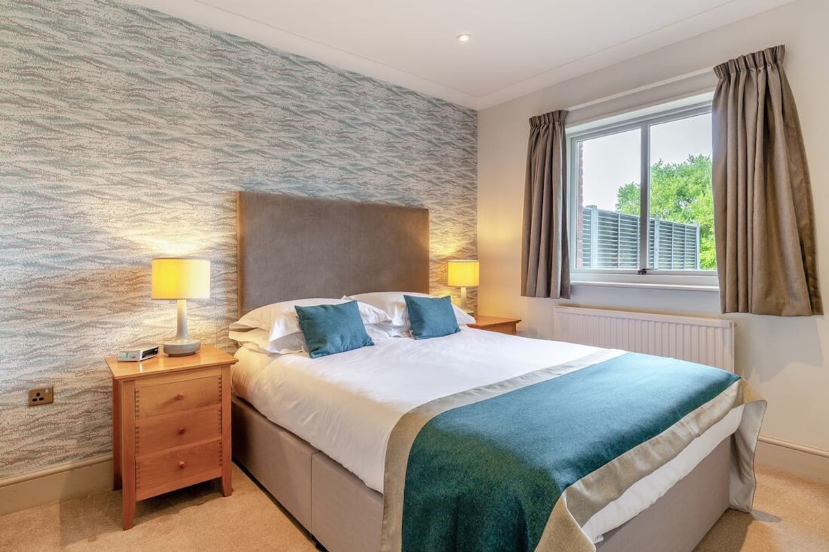 A neatly arranged bedroom with a large bed, two bedside tables with lamps, a window with curtains, and a textured wall.