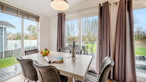 A dining area with a table, chairs, a bottle of champagne, and a bowl of fruit. - Landal Bude Coastal Resort (Bude)