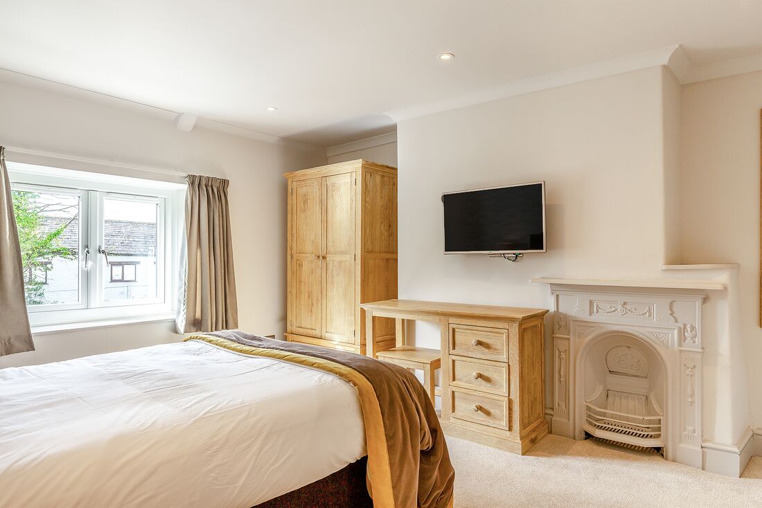 Une chambre à coucher avec un lit, une armoire en bois, une télévision, une cheminée et une fenêtre avec des rideaux.