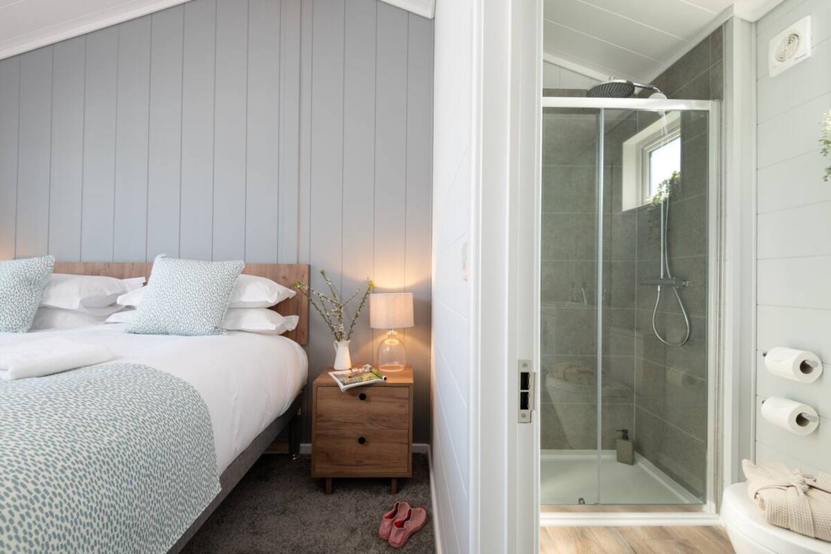 A bedroom with a bed, bedside table, lamp, and a glass-enclosed shower area.