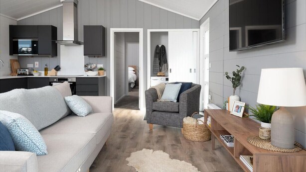 A modern living room with a sofa, a grey armchair, and a wooden side table with a lamp. - Landal Bude Coastal Resort (Bude)