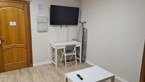 Et værelse med et træskab, et hvidt skrivebord med stol, et ophængt fjernsyn og en radiator.