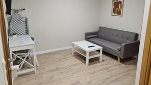 Et værelse med en grå sofa, et hvidt sofabord og et hvidt skrivebord med stol.