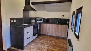 A compact kitchen with a microwave, oven, and sink. There is a wooden door with glass panels and a window on the right. - Wonderful 2-bedroom apartment in Évette-Salbert perfect for relaxing stay (Évette-Salbert)