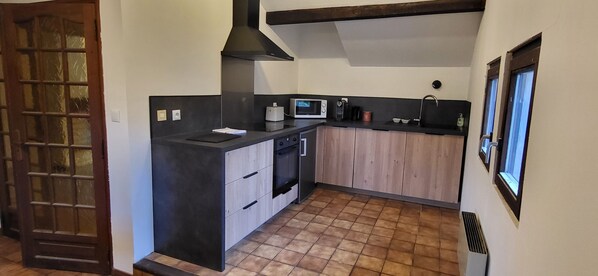 A compact kitchen with a microwave, oven, and sink. There is a wooden door with glass panels and a window on the right.