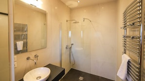 Ein modernes Badezimmer mit einem großen Spiegel, einem Waschbecken, einer Dusche inklusive Handbrause und einem Handtuchhalter.