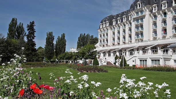 Ein großes, weißes Mehrstöckhotel mit symmetrischer Fassade, umgeben von gepflegten Gärten und hohen Bäumen.