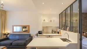 Eine moderne Küche mit einer zentralen Kochinsel, einem Essbereich mit Hockern, einer Sitzecke mit Sofa und einem großen Spiegel.