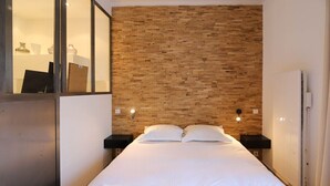 Ein Hotelzimmer mit einem hölzernen Kopfteil, einem Bett mit weißer Bettwäsche, zwei Nachttischen und einem Beistelltischchen mit einer Lampe.