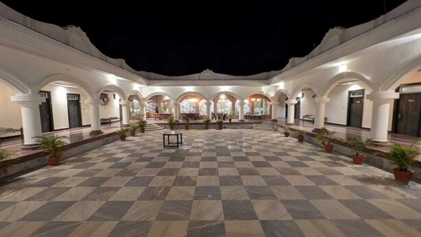 A spacious courtyard with a checkered floor, white columns, and potted plants. - Sanjay Resort Baghela Heritage (Majhauli)