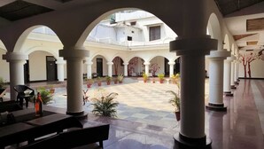 A spacious courtyard with a checkered floor, white columns, and potted plants. - Sanjay Resort Baghela Heritage (Majhauli)