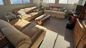 En stue med beige sofaer, et sofabord, et fjernsyn og et træskab.