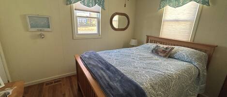 A bedroom with a wooden bed, a ceiling fan, a window with shutters, a mirror, and a small window with a view of the outside.