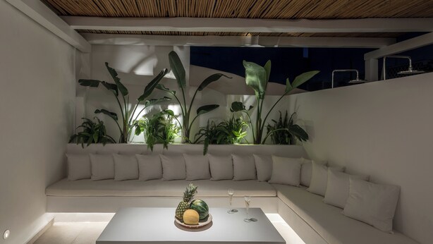 Un espacio al aire libre moderno con un sofá blanco, una mesa de centro con fruta y plantas en macetas.