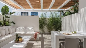 Un espacio exterior moderno con un sofá blanco, una mesa de comedor y un techo con listones de madera.